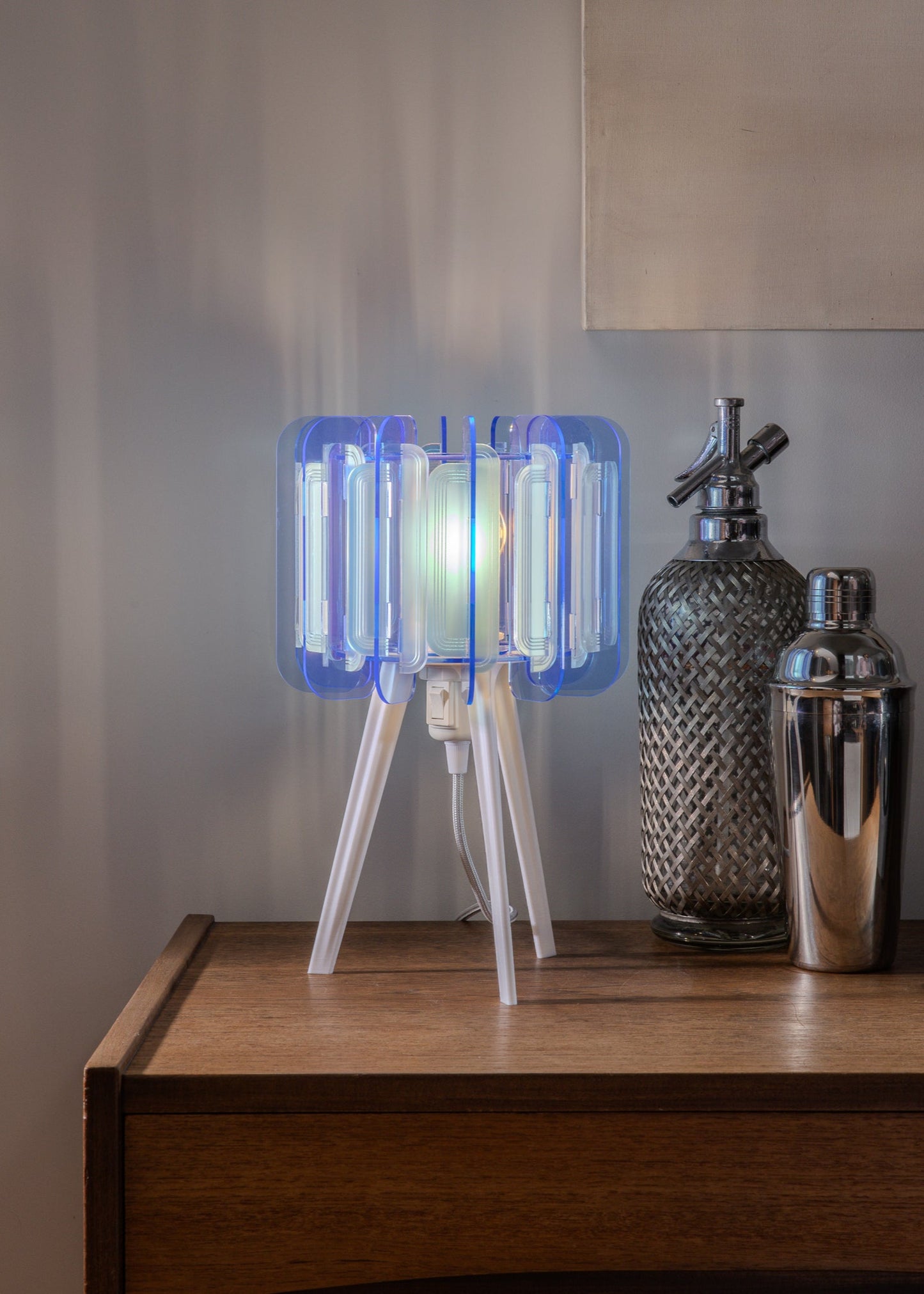 A wide shot of a stylish, modern flat with the Mini Poppy lamp on a white tripod base. The warm glow and sculptural shape stand out against clean lines and minimal furniture, highlighting its role as a statement piece in contemporary home decor.