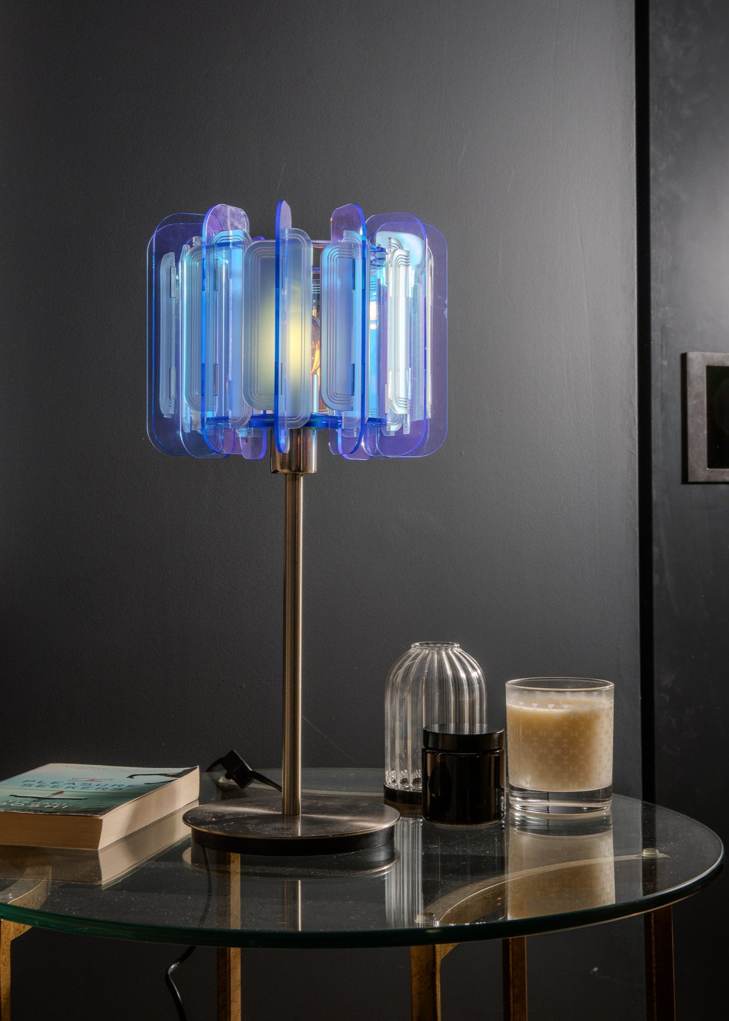 The Frosted Iridescent Mini Poppy lamp glows from a sleek silver base on a midcentury-style sideboard. Its space-age design and subtle rainbow reflections bring a chic, futuristic edge to the modern apartment setting. Ideal for design lovers and stylish city living.