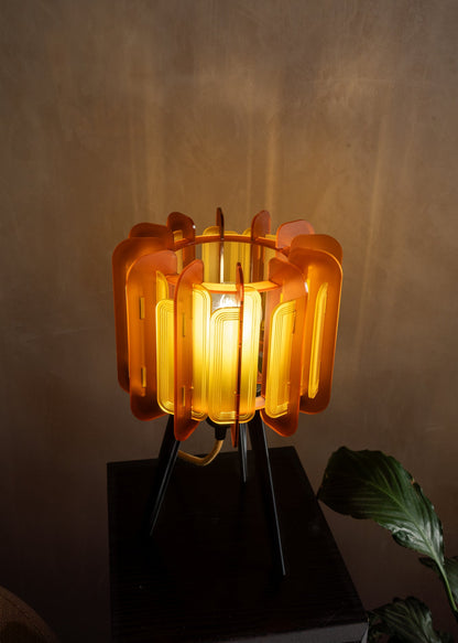 Close-up of the Saffron Mini Poppy lamp glowing softly on a bedside table. The golden yellow acrylic casts a warm, ambient light — perfect for midcentury-inspired bedrooms, boho interiors, and colour-rich design schemes.

